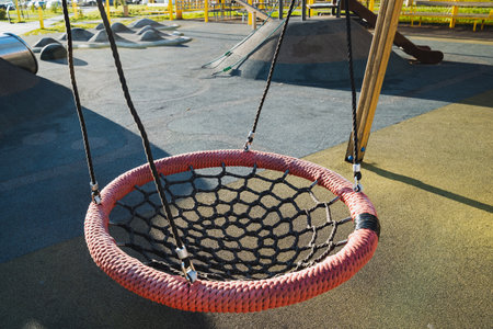 In the charming playground, a vibrant and bright red net swing warmly invites children to come and...