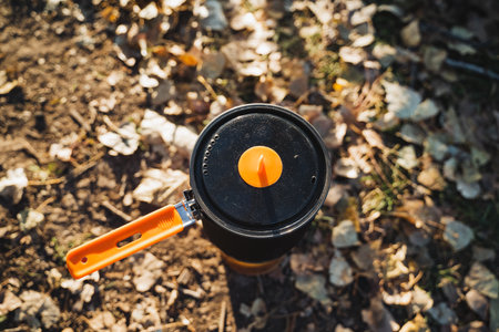 A shiny black pot with an orange handle rests on a colorful pile of autumn leaves, blending beautifully with the scenery, creating a captivating scene that invites appreciation of natures beautyの写真素材