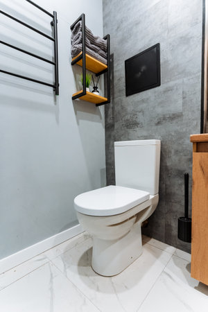 A sleek, modern bathroom design beautifully showcases a stylish white toilet, paired with shelves that hold neatly arranged towels, all set against a contemporary grey backdropの写真素材