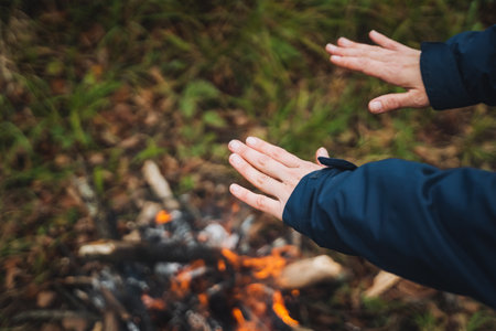 Closeup of hands warming by a campfire amidst nature, showcasing a cozy outdoor moment, perfect for camping and adventure themesの写真素材