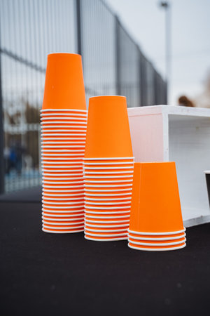 On a dining table, three vibrant orange cups are stacked together, creating a striking display that highlights their bold color and shape, enhancing the tables aestheticの写真素材