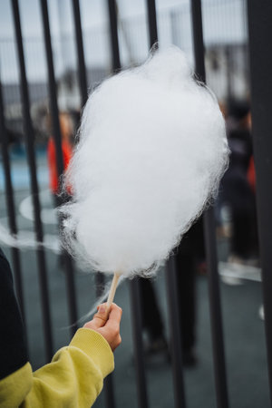 A cheerful, happy person holds a large, colorful cotton candy treat in front of a rustic wooden...