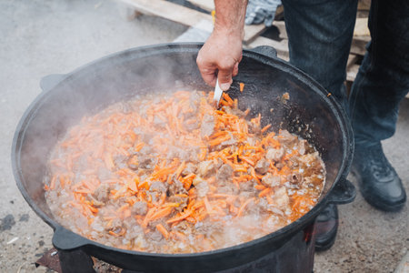 A dedicated man meticulously stirs a pot filled with simmering ingredients using a fork, intensely focused on crafting a perfectly blended and delicious meal that everyone can enjoy togetherの写真素材