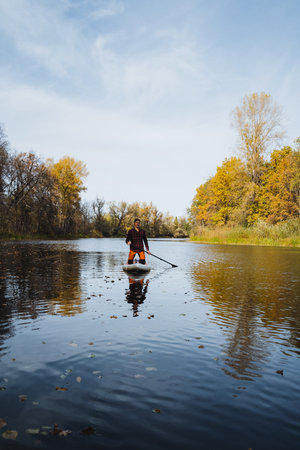 A man is enjoying a serene and relaxing paddle board ride on a calm river, fully taking in the stunning beauty of nature all around him, along with the peaceful and tranquil watersの写真素材