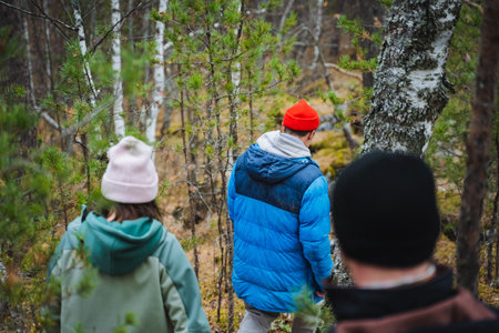 A diverse group of people is leisurely walking together through a lush forest, enjoying the serene...