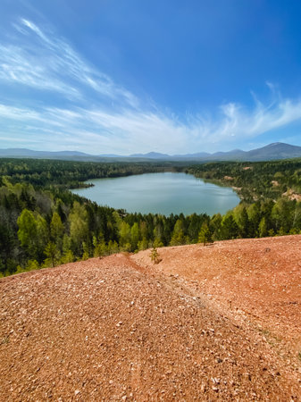 A vast and expansive body of water is beautifully surrounded by lush green trees and a mixture of dirt and gravel terrain, creating a serene natural environment that invites explorationの写真素材