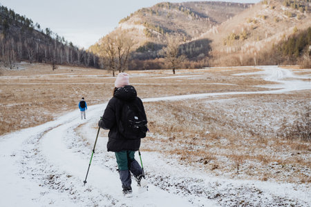 A solitary individual takes a leisurely walk along a snowblanketed trail that winds through a stunning mountainous region, encircled by soaring trees and an idyllic, tranquil natural sceneryの写真素材