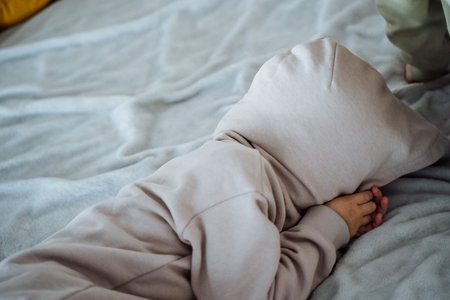 A person peacefully rests in a cozy hoodie on a soft bed, surrounded by plush linens and a warm...