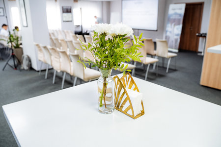 On a table within a welldesigned conference room, there is a beautiful vase filled with an...