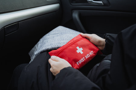 A person is comfortably sitting inside a car while holding a bright red first aid kit, prepared for any emergencies that may arise during their time spent on the road or traveling in the vehicleの写真素材