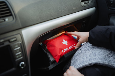 A person is carefully extracting a first aid kit from the glove box located in the interior...