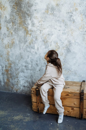 A little girl is sitting comfortably on a wooden box, perhaps lost in thought or enjoying her surroundings, with her little knees folded beneath her, absorbed in her own little worldの写真素材