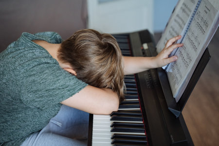 A frustrated young musician struggles at the piano with sheet music, highlighting the challenges and dedication in their creative journey to master their craftの写真素材