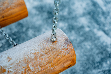 A beautiful wooden swing, complete with chains, is completely covered in a soft layer of white snow,...