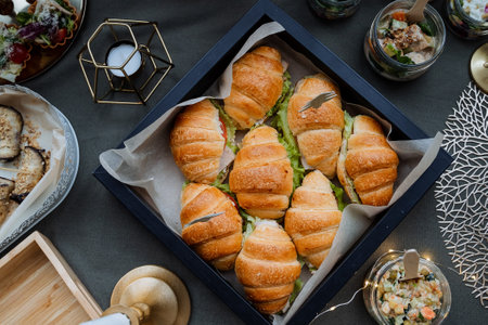 A beautifully arranged box on the table is filled with delicious croissants and assorted sandwiches, ready to be enjoyed by everyone at this delightful gathering, bringing joy to allの写真素材