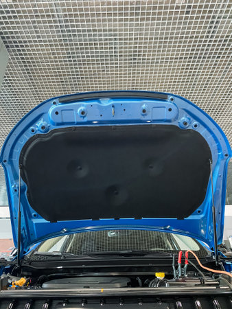 The hood of a shiny blue car is propped open, revealing the intricacies of the engine underneath,...