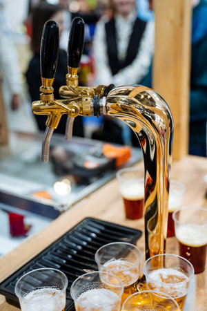 A shiny beer tap pours cold beer into neatly arranged glasses, creating a warm atmosphere appealing to those who enjoy good drinks and vibrant gatherings with friends and loved onesの写真素材
