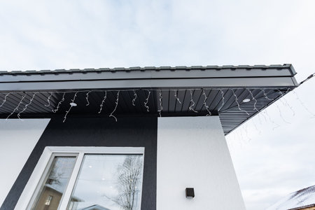 The charming roof of the house is beautifully adorned with vibrant and colorful Christmas lights,...