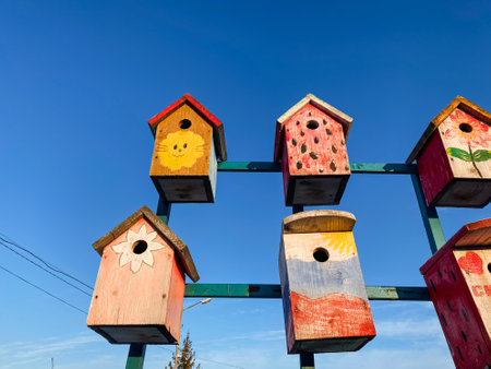 A delightful collection of vibrant and colorful bird houses is beautifully hanging from a sturdy pole, creating an enchanting and whimsical display against the backdrop of a stunning clear blue skyの写真素材
