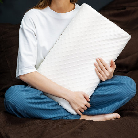 A woman is comfortably sitting on a soft and inviting couch, gently holding a fluffy white pillow in her hands as she enjoys her muchneeded relaxation time and unwinds in her cozy living spaceの写真素材