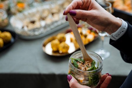 A woman is holding a jar filled with delicious food, using a wooden spoon in her hand to perhaps serve or prepare it. The scene is likely involving cooking or meal preparation activitiesの写真素材