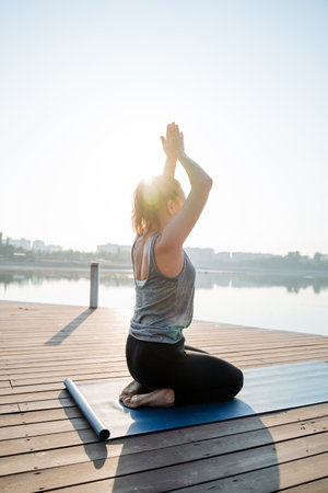 A woman kneels on a soft yoga mat on a serene dock, immersed in natures calming sounds and the gentle lapping of tranquil lake waters, creating a peaceful practice atmosphereの写真素材