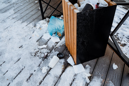 A trash can is placed on a wooden deck that is completely blanketed in a thick layer of fresh, glistening snow, creating a winter scene made up of contrasting elementsの写真素材