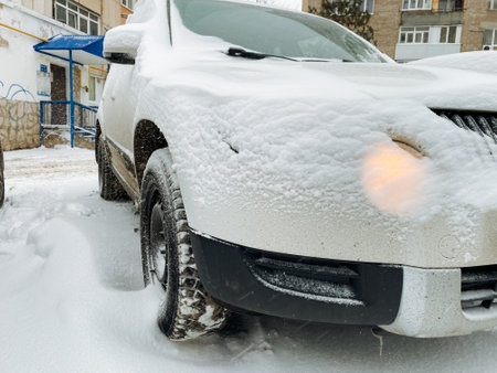 In the expansive parking lot, there sits a white car that has been completely obscured by a thick layer of fresh snow, transforming it into a beautifully wintery and picturesque sight to beholdの写真素材