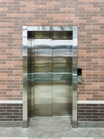 A sleek stainless steel elevator stands in close proximity to a sturdy brick wall, creating a...