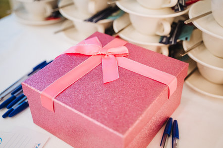 A beautifully arranged dining table showcases an exquisite pink gift box, adorned with a delicate pink ribbon, which enhances the enchanting decor and inviting atmosphere of the settingの写真素材