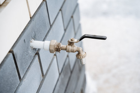 This image captures a closeup view of a single faucet mounted on a rough, textured brick wall, highlighting the contrast between the shiny metal of the faucet and the rugged brick surface behind itの写真素材