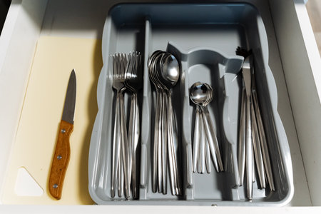 A drawer that is filled with various pieces of silverware, including an assortment of spoons, forks,...