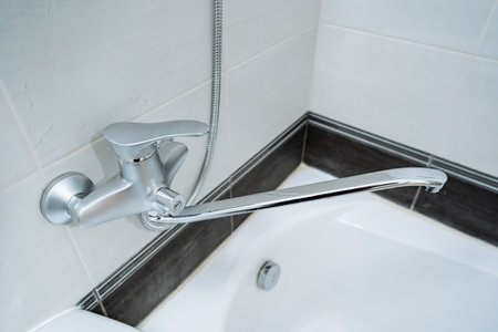 This image features a closeup view of a shiny bathtub faucet located in a stylish and modern...
