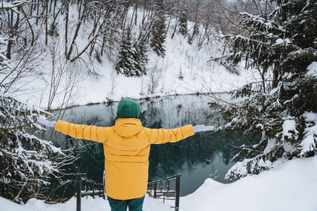 A person wearing a bright yellow jacket is standing in the beautiful snow, with their arms fully...