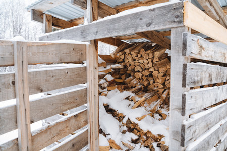 In a rustic wooden shed, a neat stack of freshly cut wood is nestled under a soft white blanket of snow, beautifully highlighting the charm and serene beauty of the cold winter seasonの写真素材