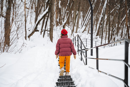 A solitary person is walking slowly down a narrow, snowy path in the tranquil, peaceful woods, surrounded by tall, majestic trees, creating a truly unforgettable winter adventure experienceの写真素材