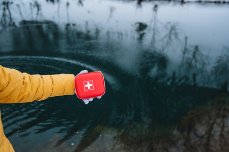 A person is seen holding a first aid kit above the water. This kit is essential safety gear that is indispensable for various outdoor activities and adventuresの写真素材