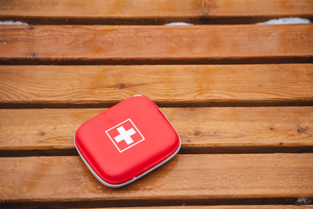 A Compact Red First Aid Kit is placed on a Wooden Surface, ready for use in various Emergency Situations that may arise during your outdoor activities or daily life routinesの写真素材