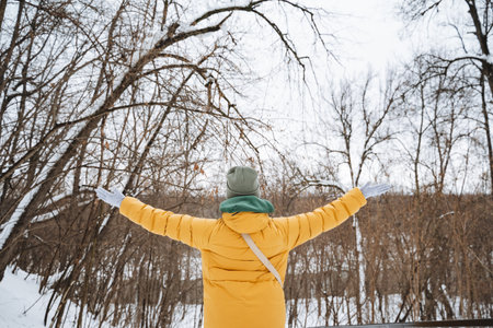 A woman wearing a bright yellow coat is standing gracefully in the soft, white snow while joyfully stretching her arms outward, embracing the chilly winter air around herの写真素材