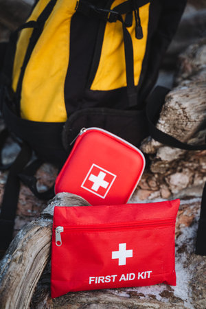 A first aid kit is positioned on a rock adjacent to a backpack, ready for any potential emergencies...