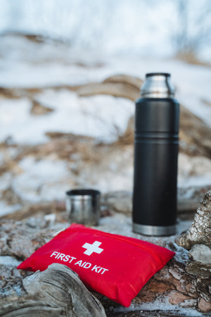 A first aid kit is placed on a rock just beside a thermos that is commonly used to keep drinks hot or cold, ensuring that essentials are readily available for emergencies or outdoor activitiesの写真素材