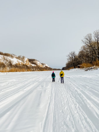 Two individuals are engaged in cross country skiing on a beautifully snowy road, surrounded by the serene winter landscape and glacial landforms that create a picturesque scene of recreationの写真素材