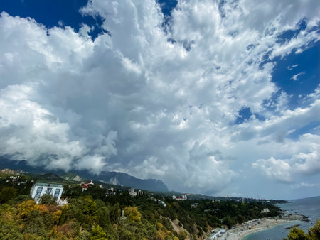 This is a stunning view that showcases a picturesque beach alongside majestic mountains, all under a sky adorned with beautiful white clouds drifting by, creating a serene and tranquil atmosphereの写真素材