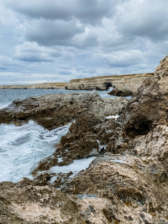 A breathtaking rocky shoreline is vividly illustrated, showcasing waves crashing against the robust rocks during a gloomy day characterized by thick, dark clouds looming ominously overheadの写真素材