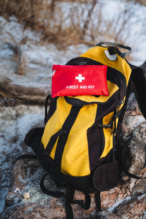 A cheerful and vibrant yellow backpack with a bright red first aid kit perched on top creates a...