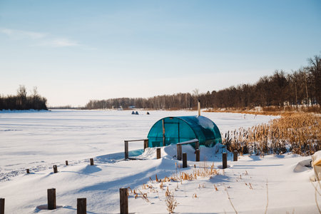 In a beautiful, snowcovered field, a greenhouse with transparent walls provides a source of warmth and refuge, and it stands out vividly against the frigid, harsh winter environment surrounding itの写真素材