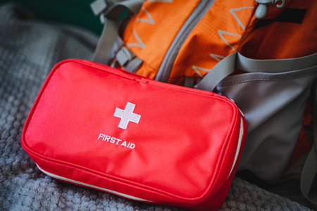 A bright red first aid kit is positioned right next to a sturdy backpack, indicating a readiness for outdoor adventures or emergencies that may arise during travel or hiking tripsの写真素材