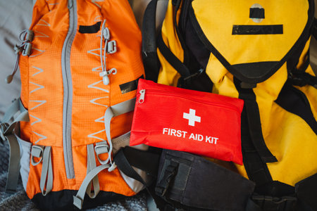 A bright red first aid kit is prominently placed on top of a vibrant yellow backpack, creating a...