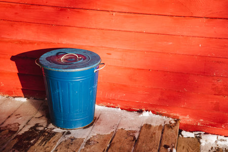 A bright blue trash can is positioned on a polished wooden floor, situated perfectly in front of a...