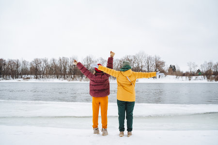 Two individuals are standing amidst the beautiful snow with their arms outstretched, enjoying the chilly atmosphere and the winter scenery all around them filled with glistening white flakesの写真素材